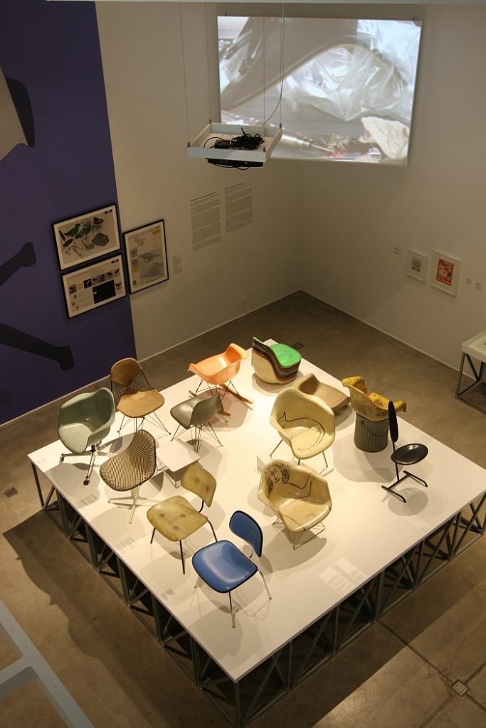 Eine Sammlung von Glasfaserstühlen - und ein Video, welches deren Produktion erklärt, gesehen bei "Charles & Ray Eames. The Power of Design", Vitra Design Museum